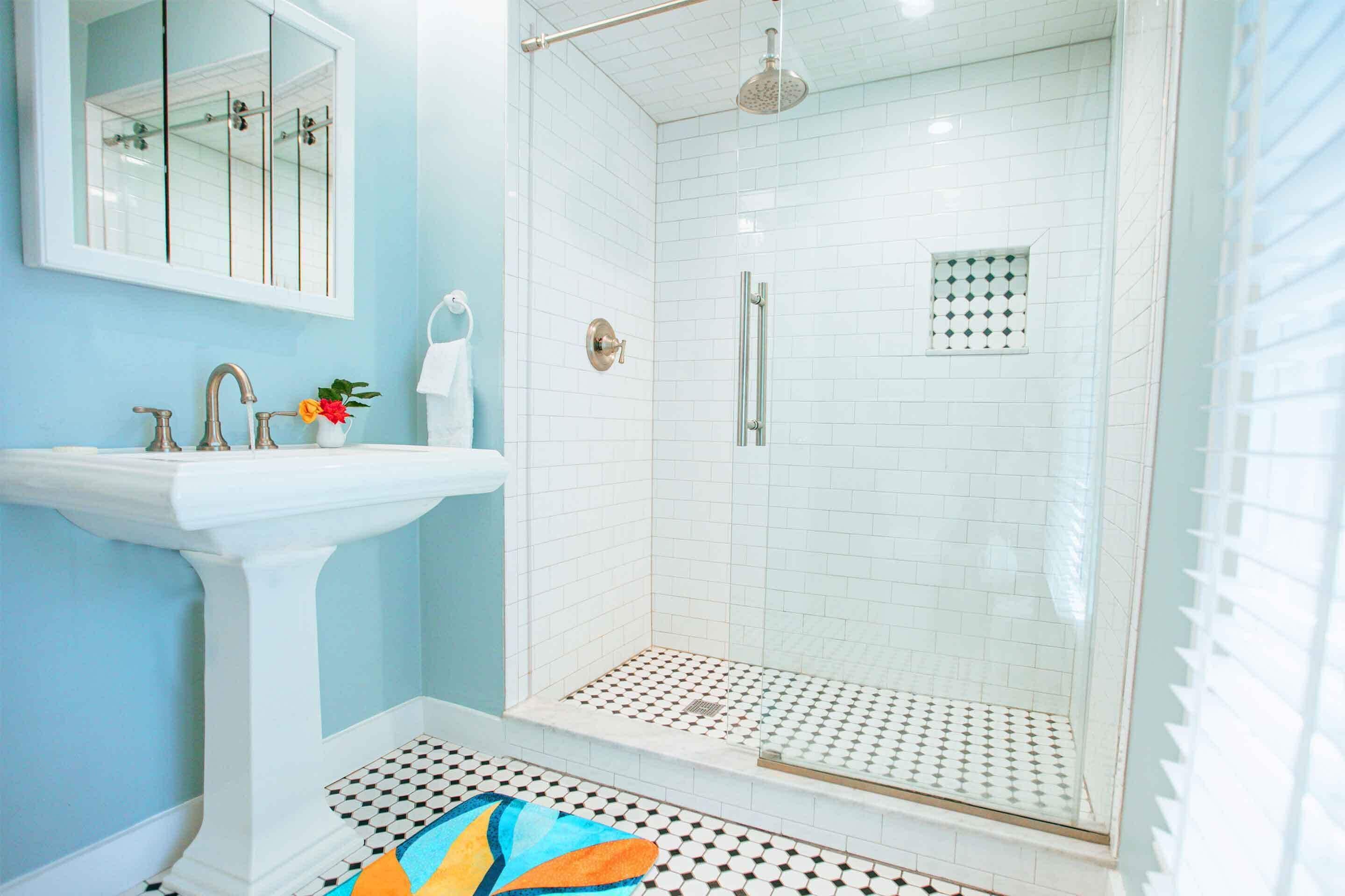 A bathroom with a white sink, a mirror, a shower with a glass door, and a patterned floor.