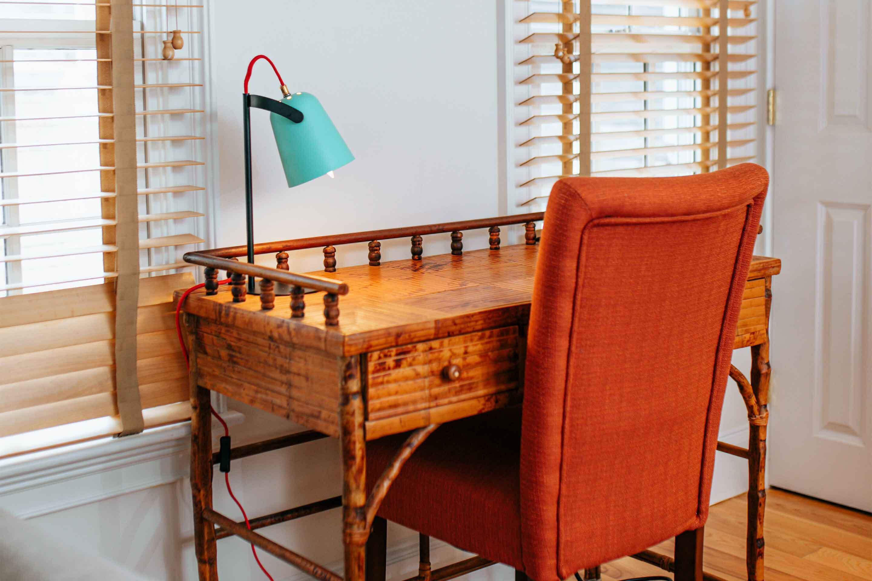 A wooden table with a drawer, a chair with a red cushion, and a teal desk lamp.