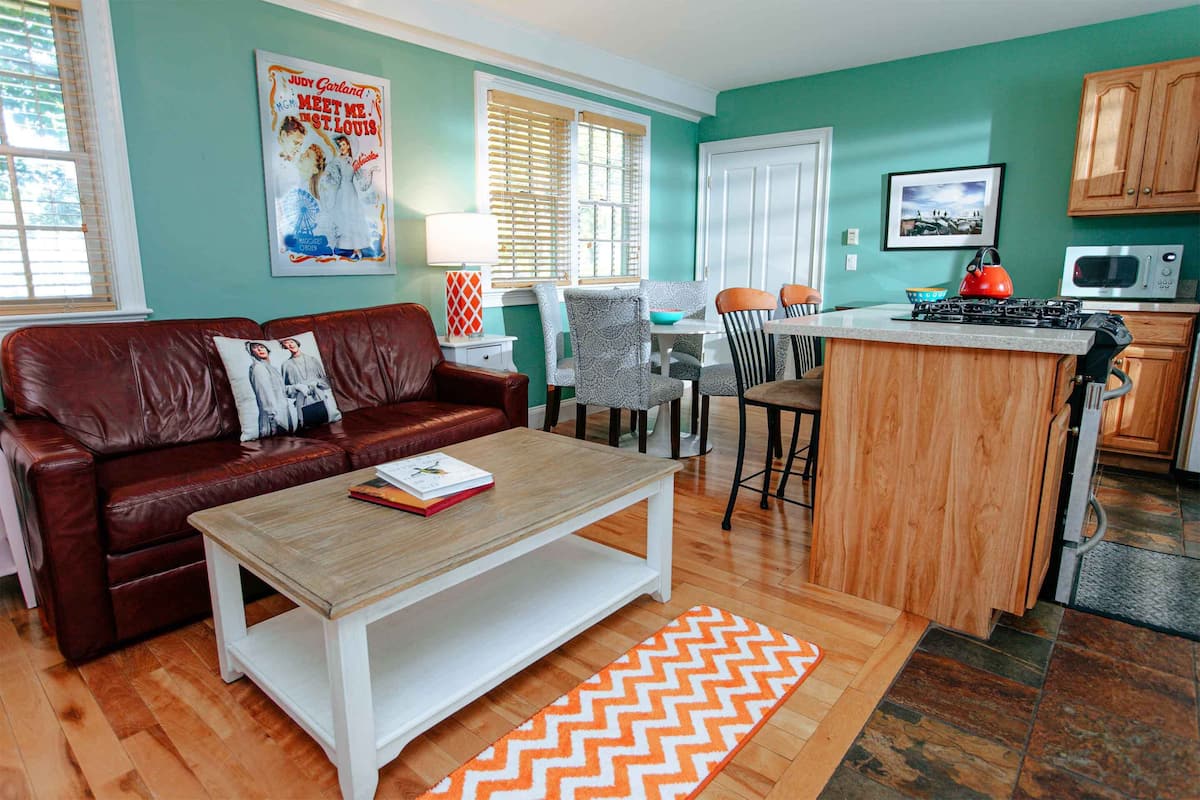 Un salón acogedor con un sofá de cuero marrón, una mesa de centro de madera y un comedor con una pequeña isla.