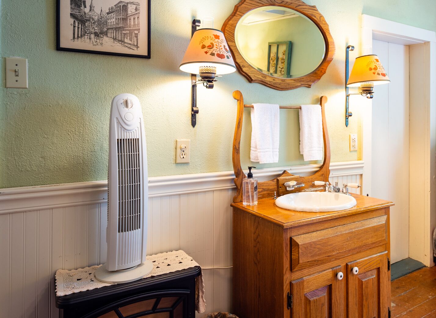A bathroom with a wooden vanity, a white pedestal heater, a mirror with a wooden frame, and two wall-mounted lamps.