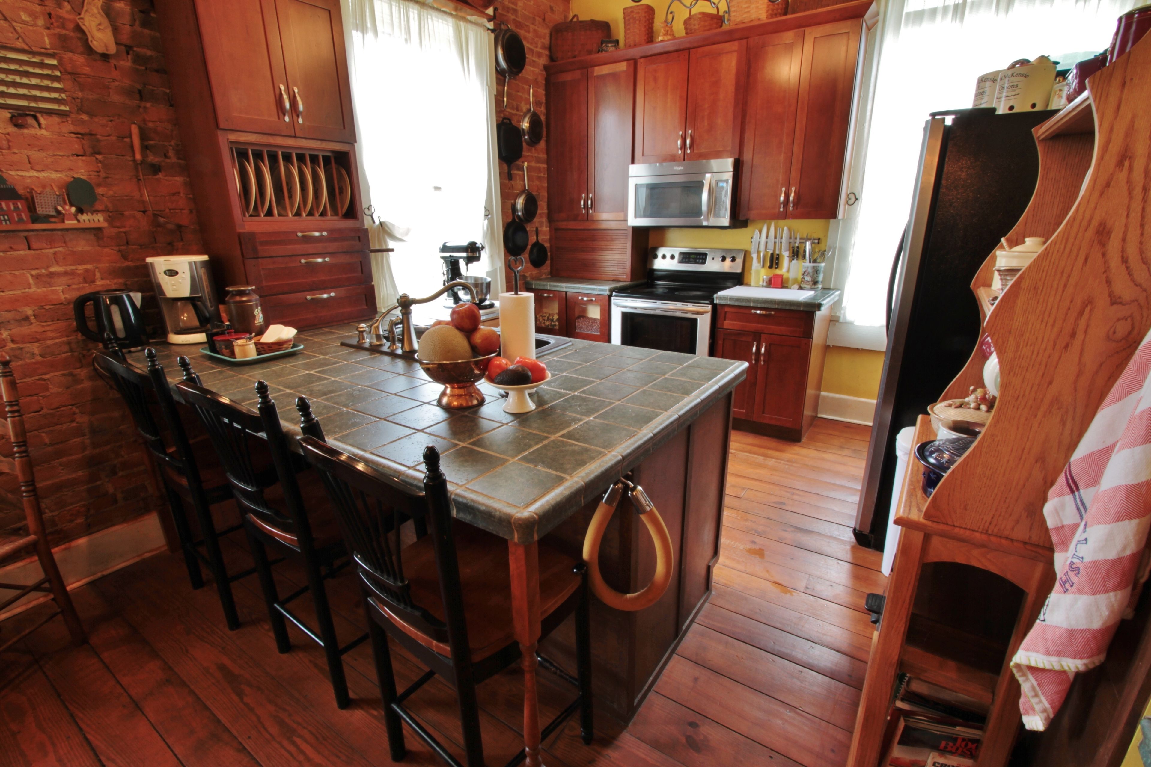 A kitchen with wooden cabinets, a large island with stools, a brick wall, and a refrigerator.