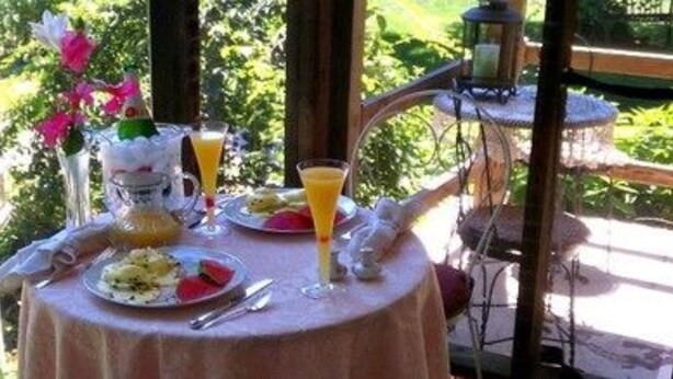 Een tafel buiten gedekt, met een tafelkleed, borden vol eten, een glas sinaasappelsap en een kaars.