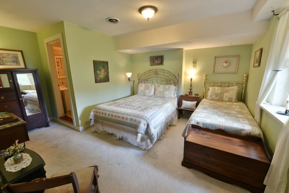 A bedroom with two beds, a dresser, a chair, and a door leading to another room.