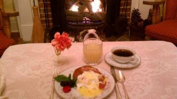 Une table mise pour le petit-déjeuner avec une assiette d’œufs, des toasts et des fruits, un verre de jus d’orange et une tasse de café, le tout posé sur une table recouverte d’une nappe à motifs.