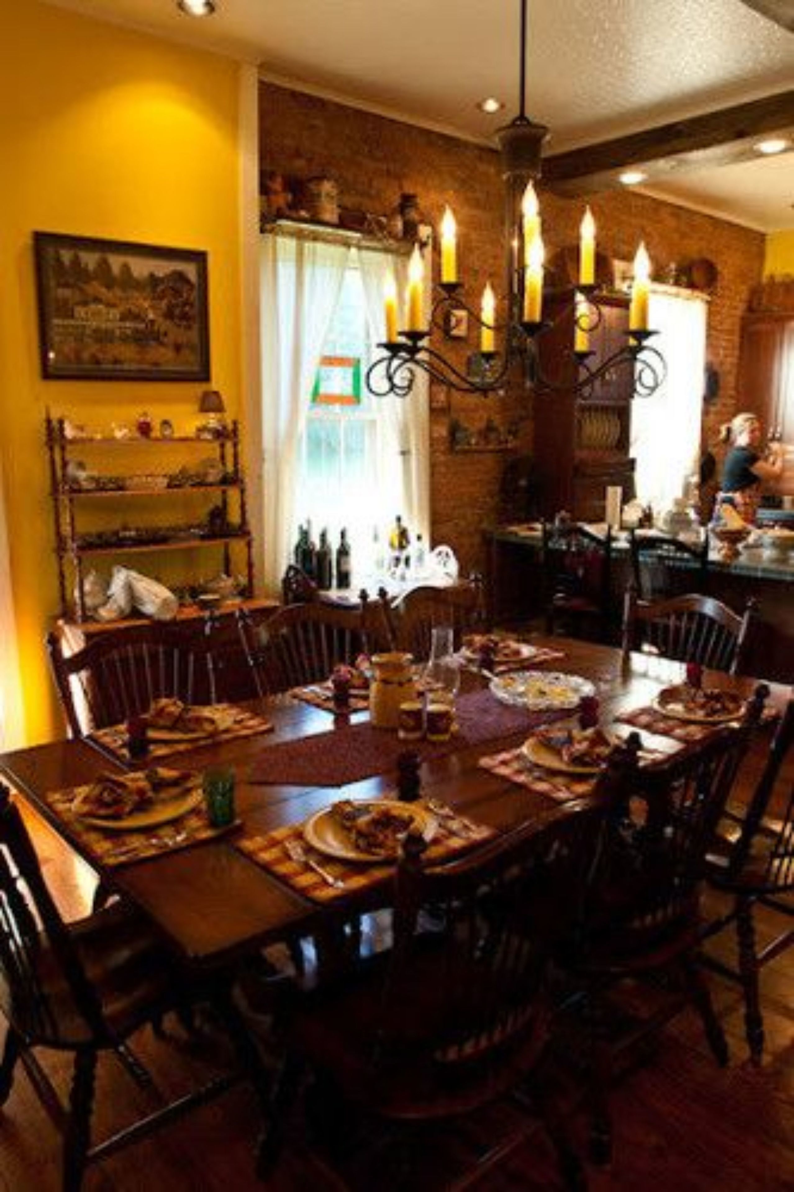 A dining room with a wooden table set for a meal, a chandelier, and a brick wall.