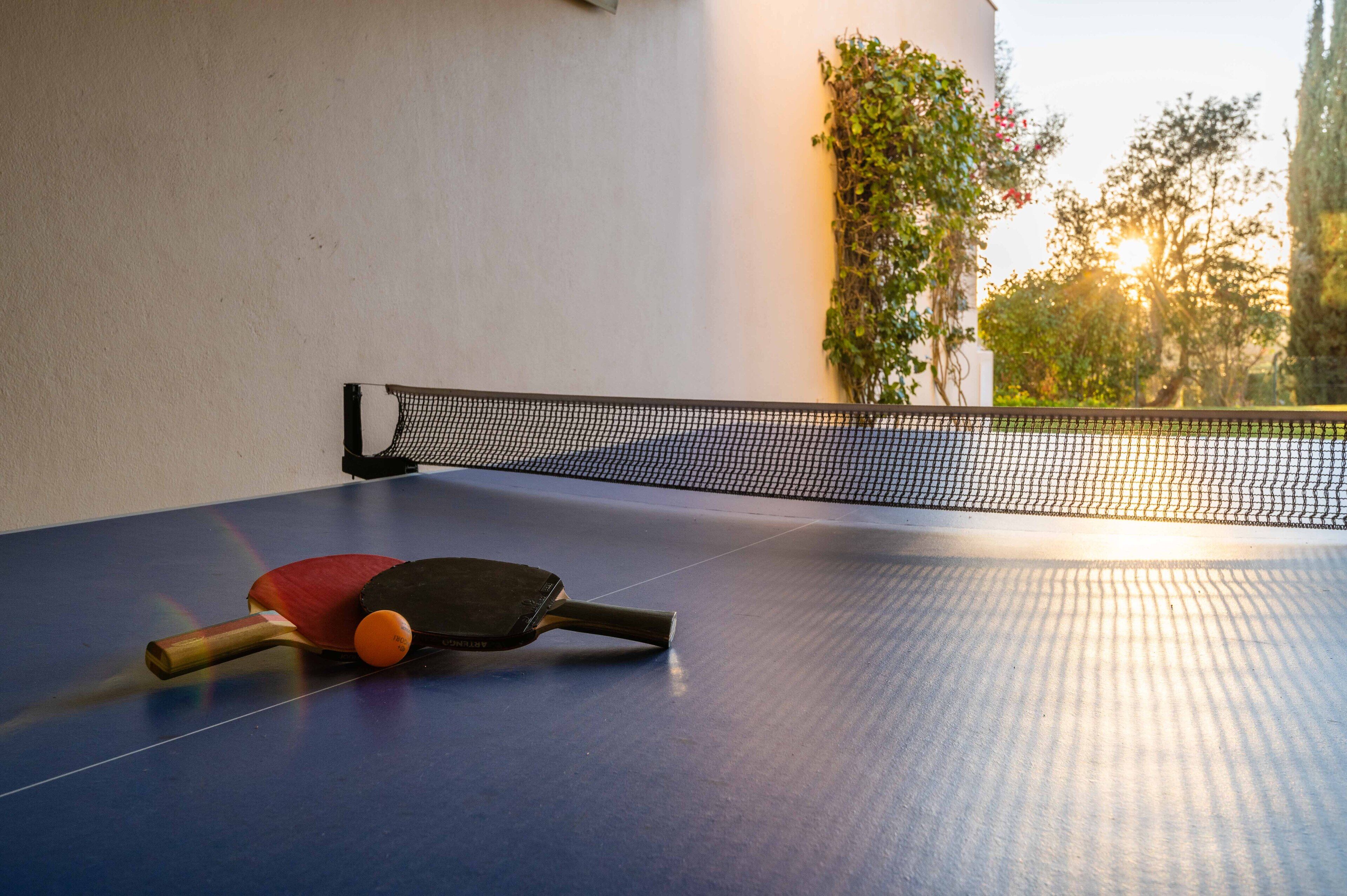 A ping pong table with two paddles and a ball, set against a wall with a net.
