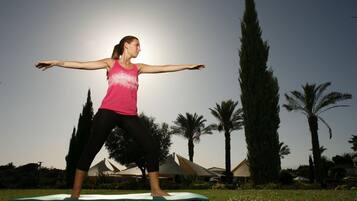 A person performing a yoga pose on a mat outdoors with palm trees and a building in the background.