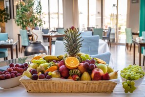 A fruit basket on a table in a dining area with chairs and tables in the background.