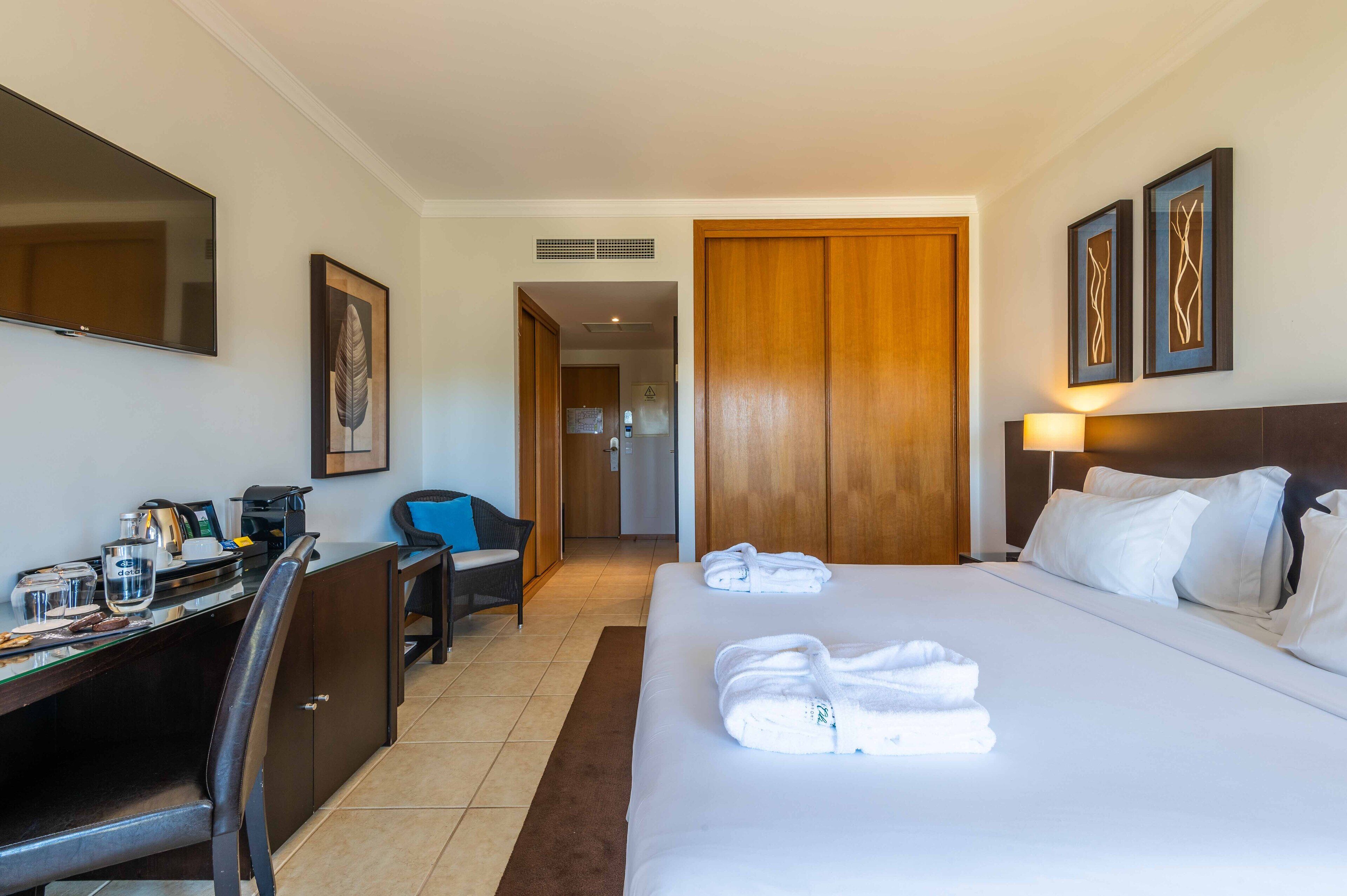 A hotel room with a bed, a desk with a computer, a chair, and a television.