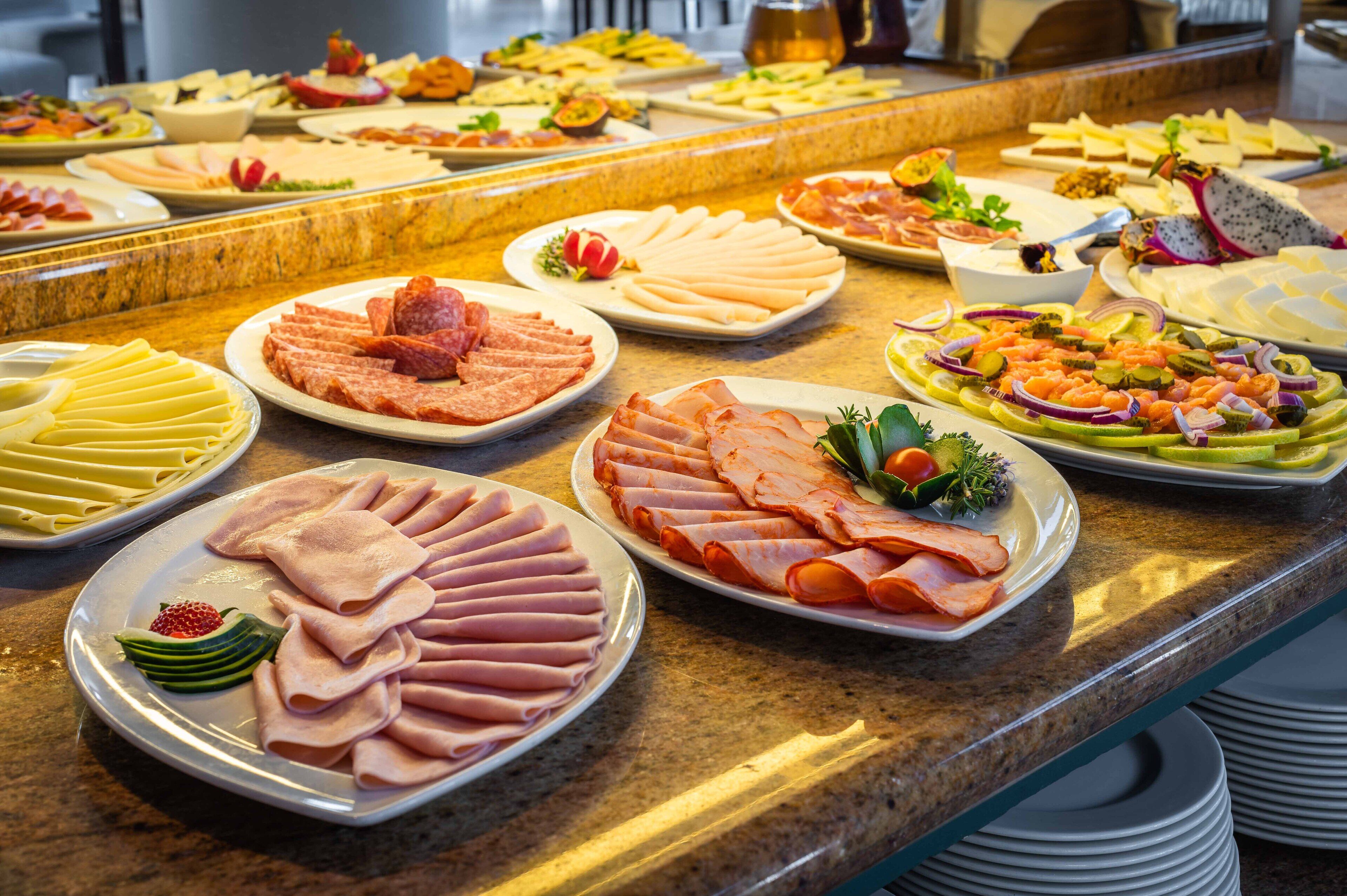 A buffet with various food items including meats, cheeses, and fruits.