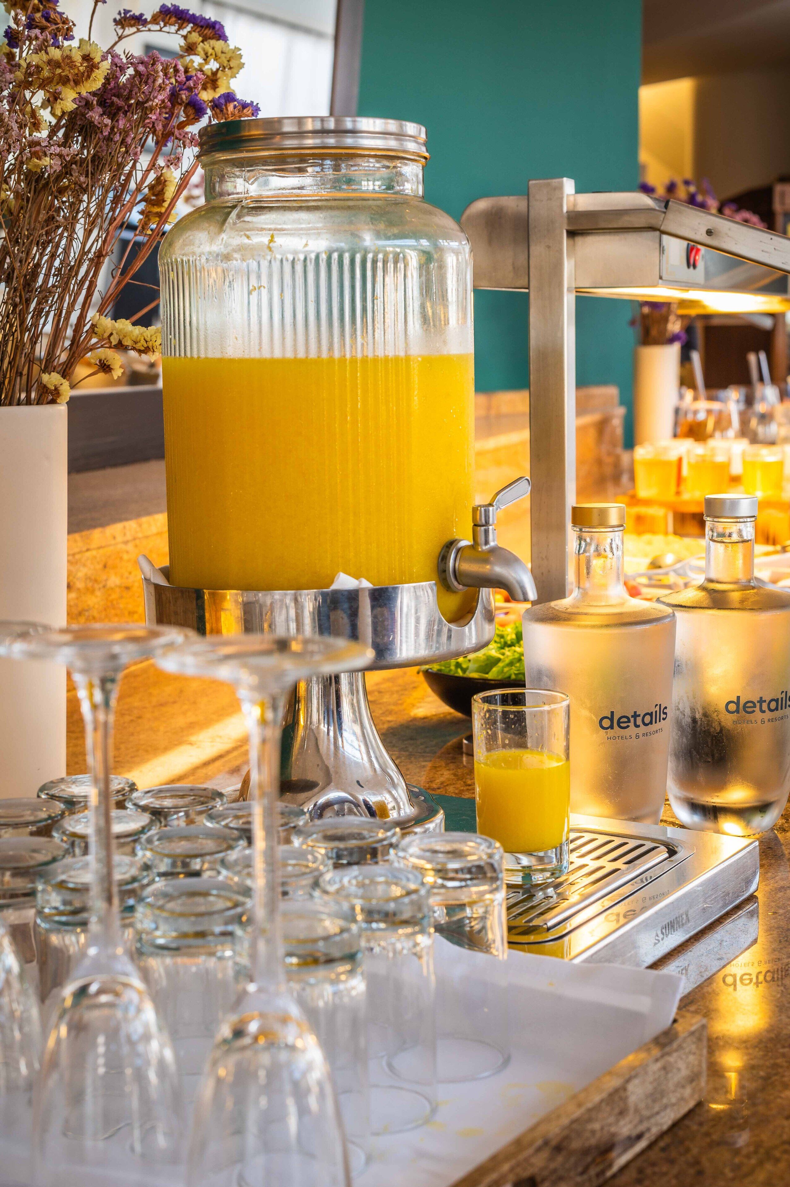 A bar area with a large glass punch bowl filled with a yellow beverage, several glasses, and bottles labeled "details" on a counter.