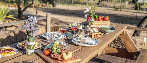 Un juego de mesa de picnic de madera al aire libre con varios platos, entre ellos comida a la parrilla, ensaladas y bebidas.