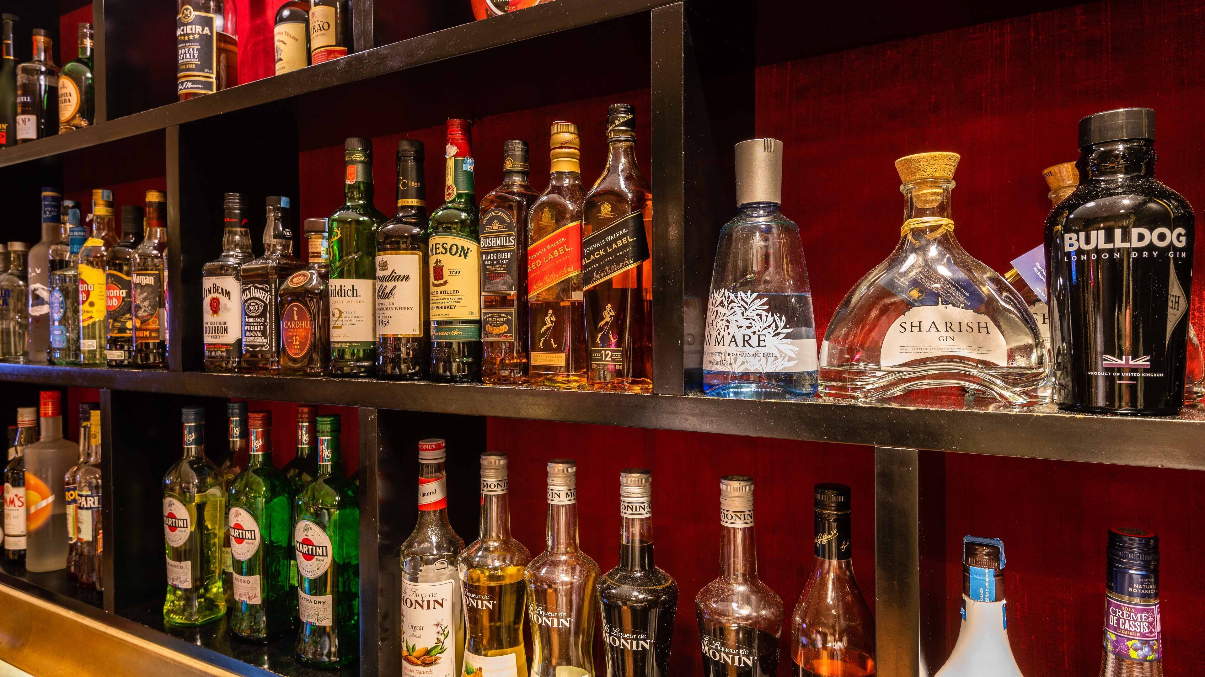 A variety of liquor bottles on shelves in a bar setting.