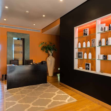 A reception area with a reception desk, a large vase with dried flowers, and a wall display of toiletries.