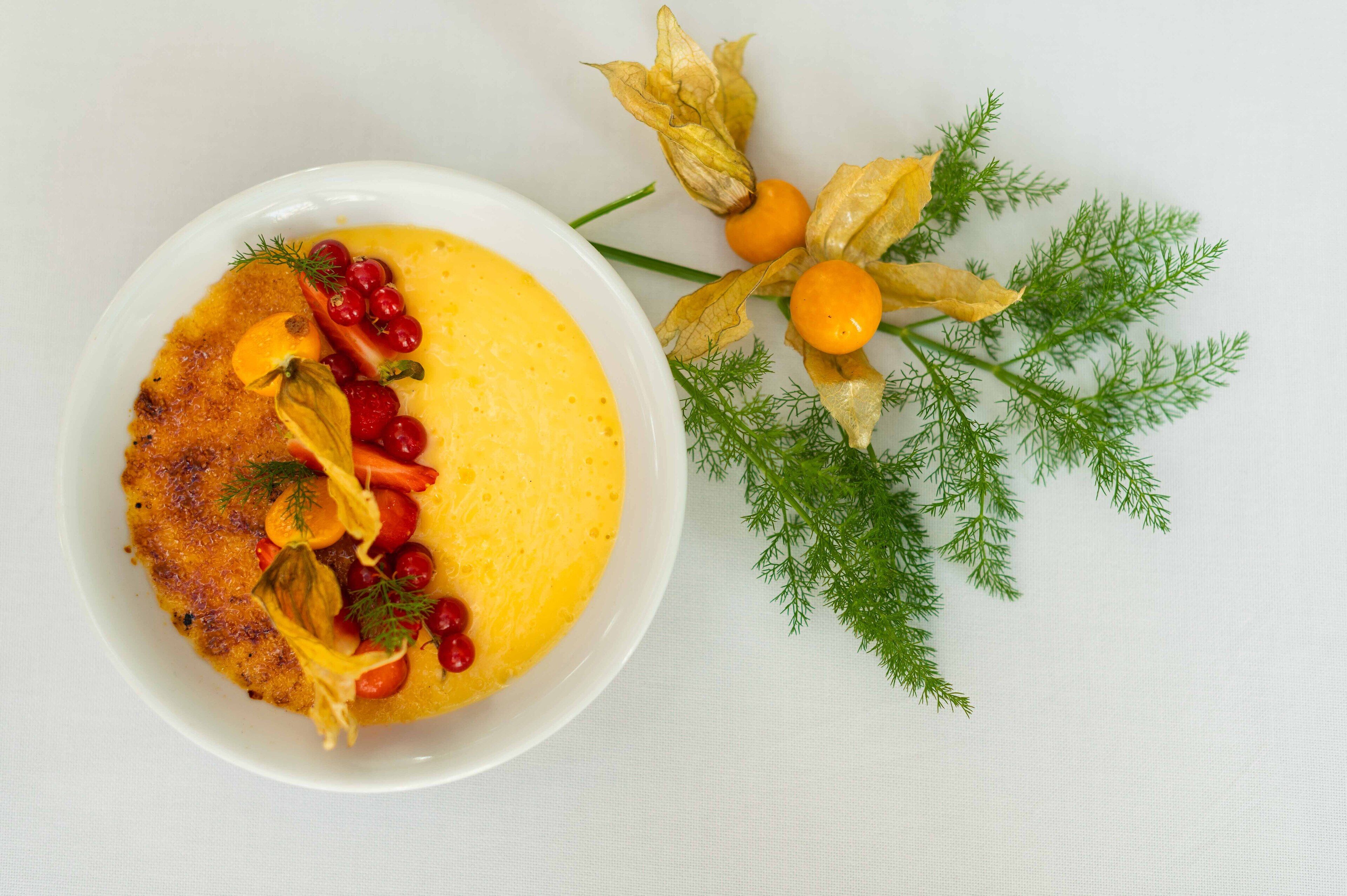 A white plate with a yellow dish, garnished with red berries and herbs, and a sprig of dill.