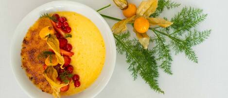 A white plate with a yellow dish, garnished with red berries and herbs, and a sprig of dill.