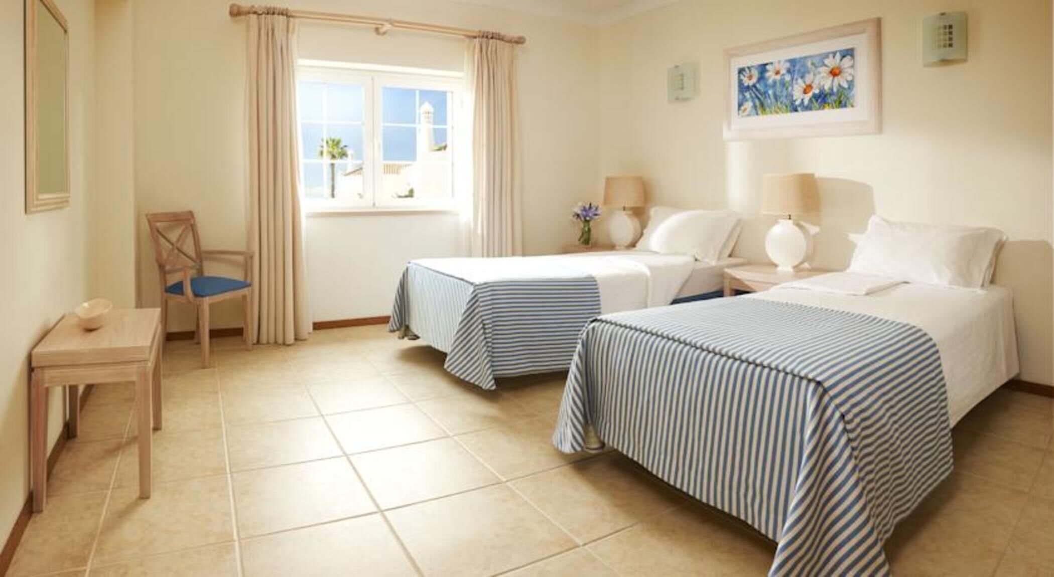 A hotel room with two beds, a chair, a small table, and a window with curtains.