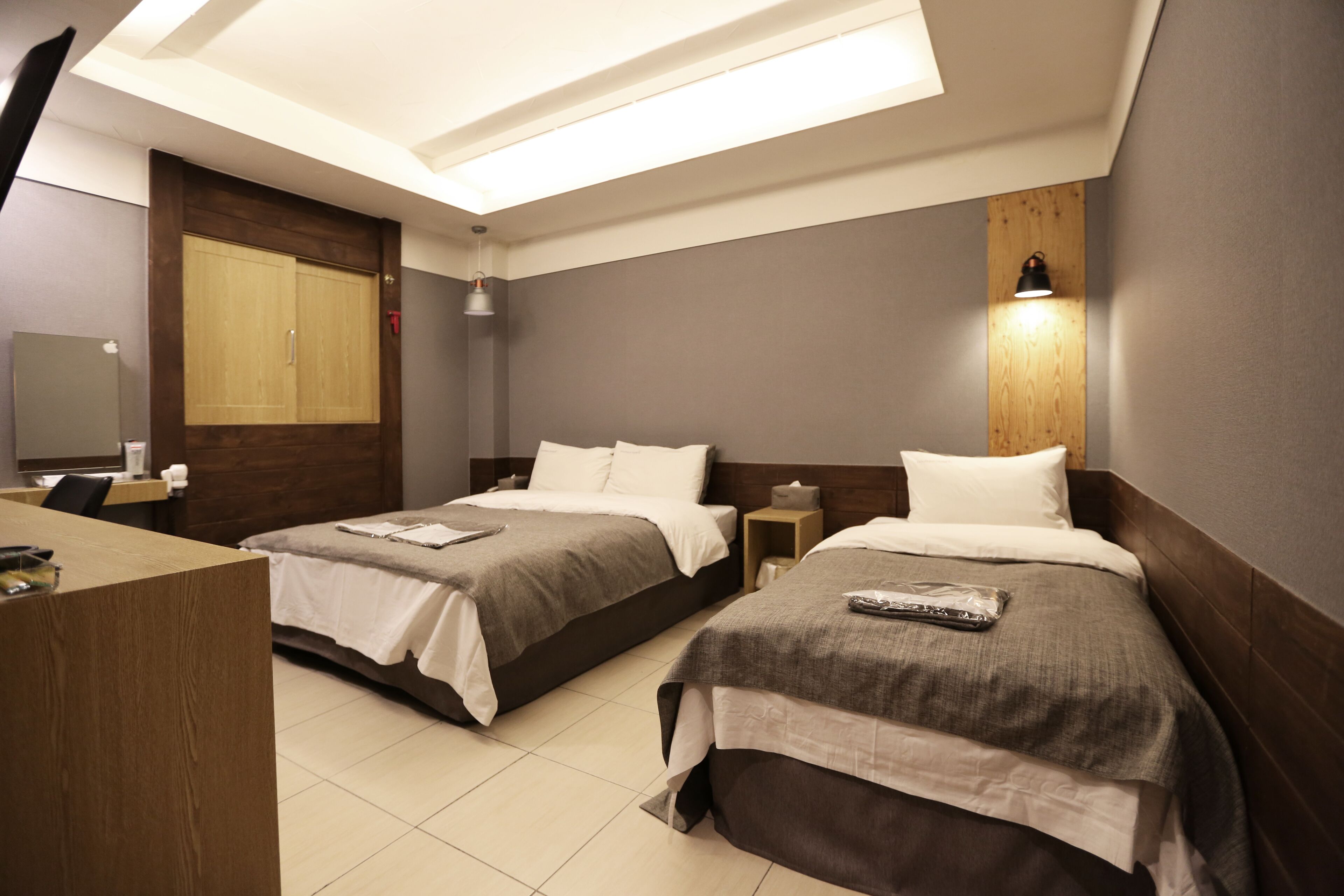A hotel room with two beds, a desk, a mirror, and a wooden headboard.