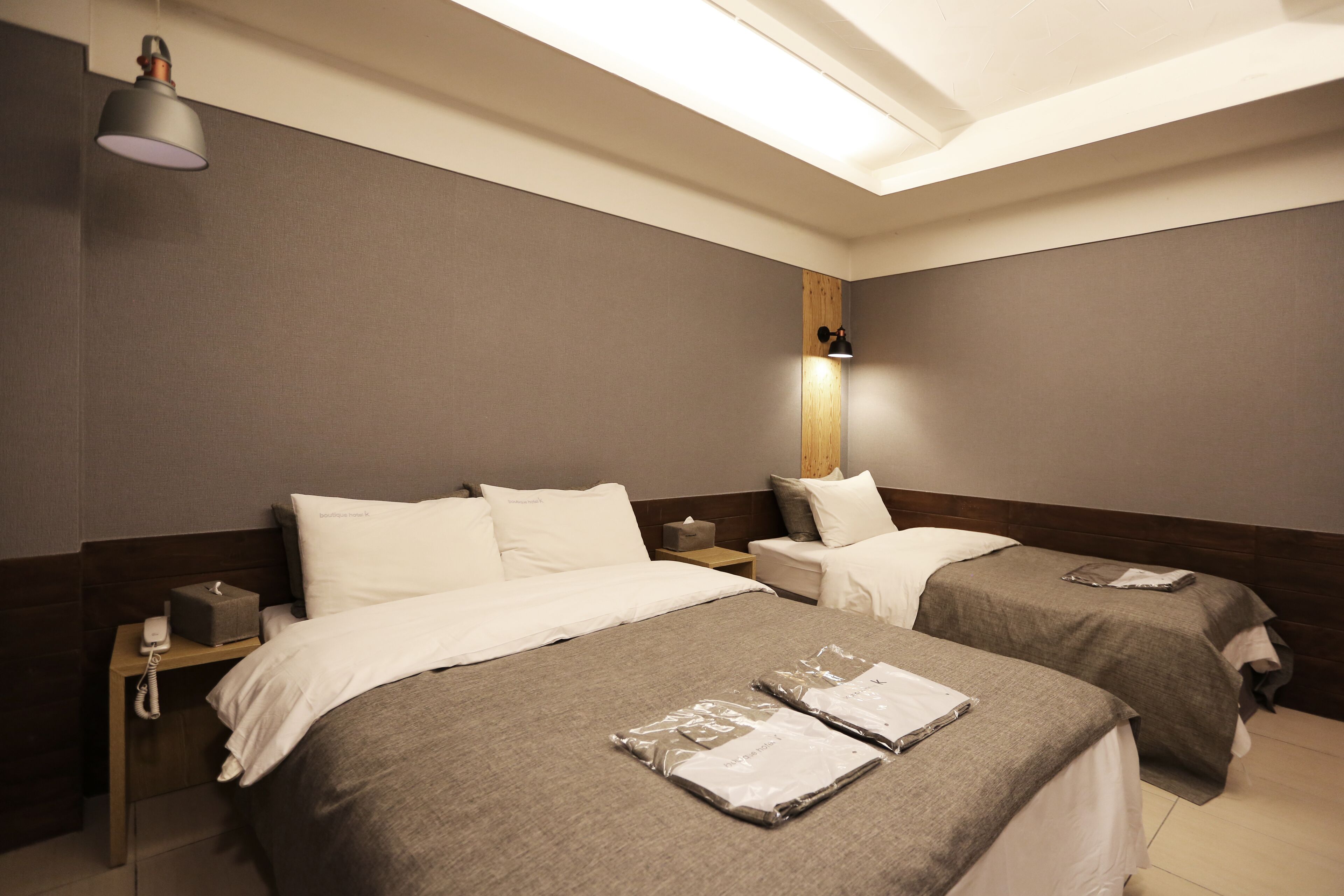 Een hotelkamer met twee bedden, een nachtkastje met lamp, een houten hoofdbord en een wandlamp.