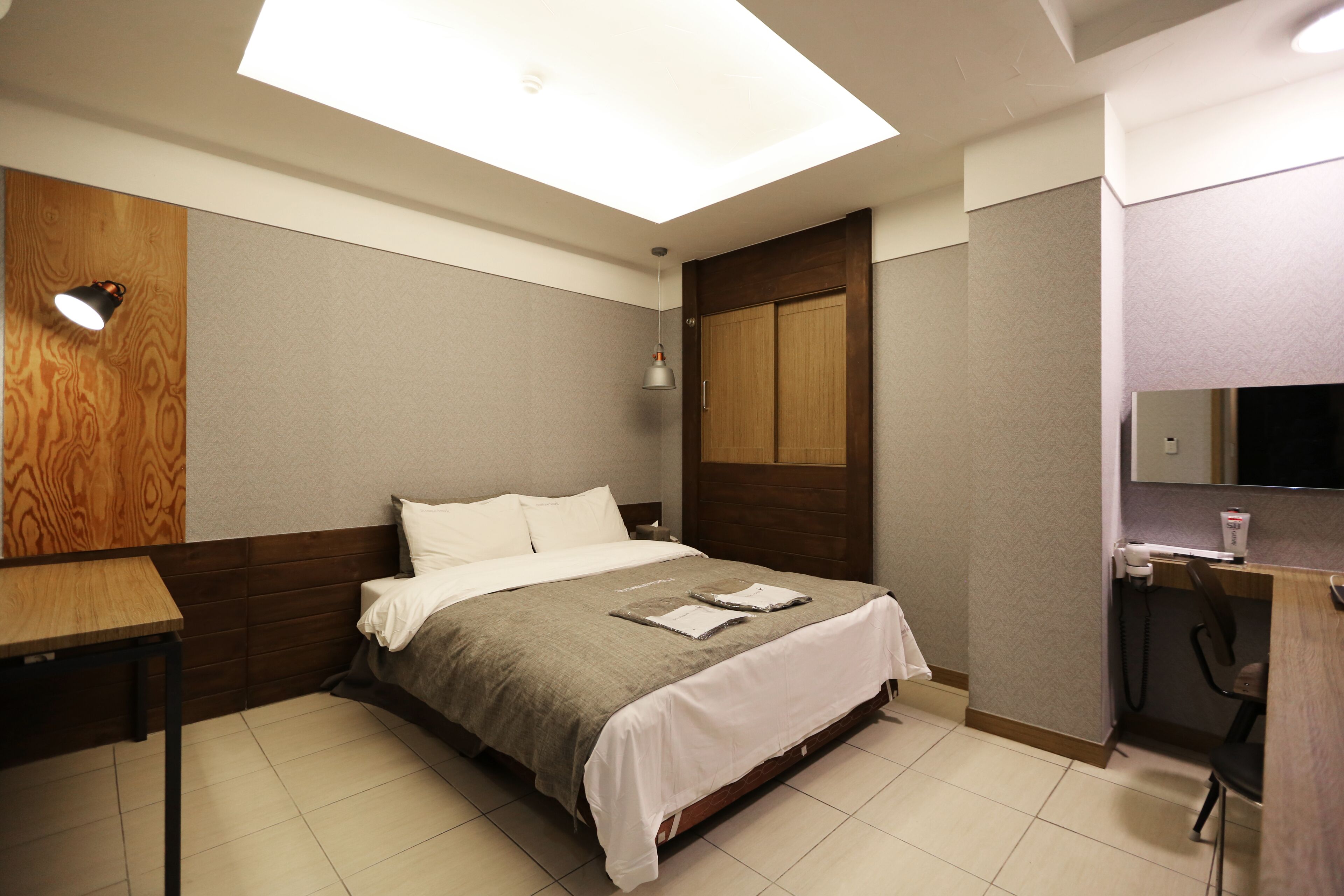 A hotel room with a bed, a desk, a mirror, and a ceiling light.