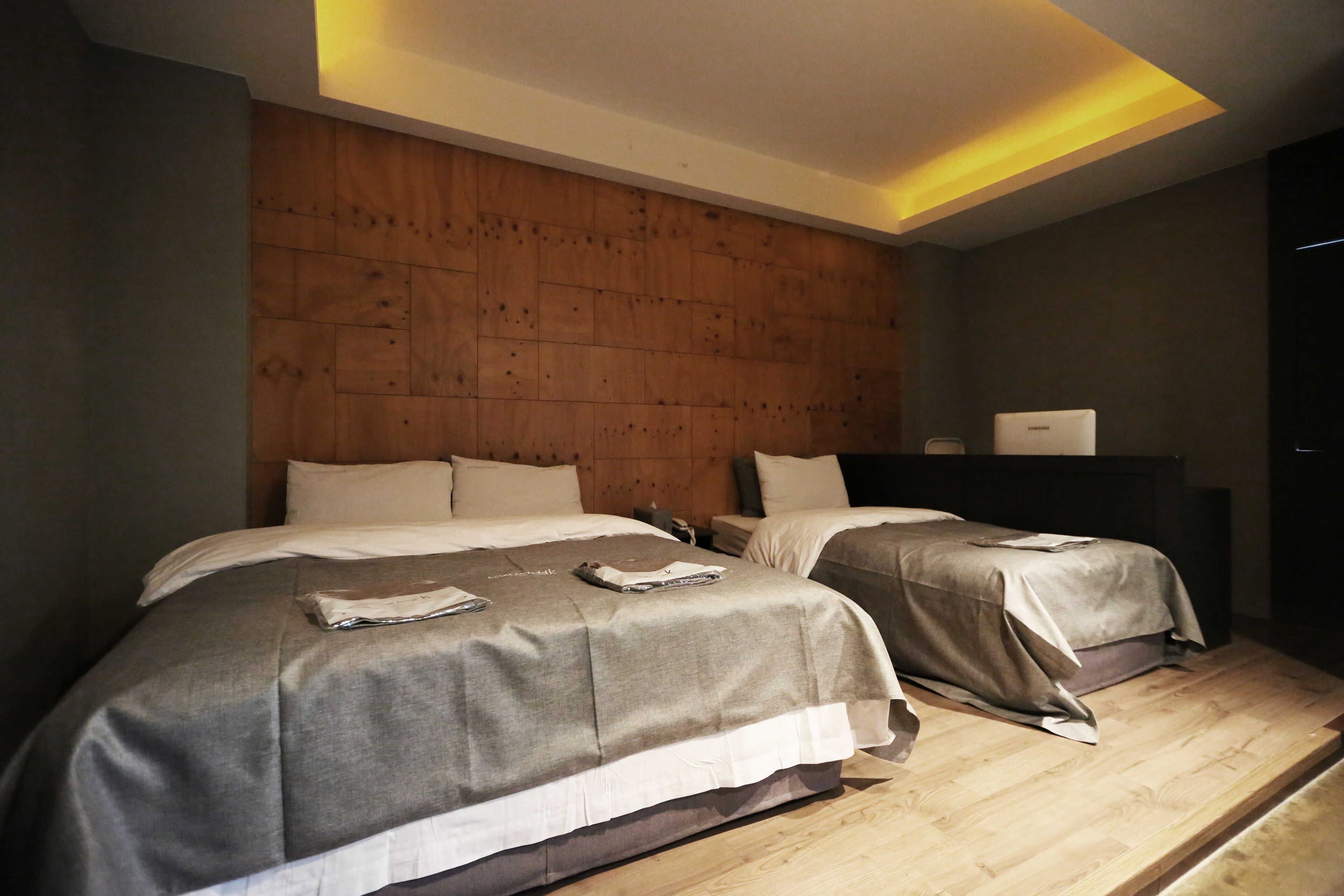 A modern hotel room with two beds, wooden headboard, and a small desk with a lamp.