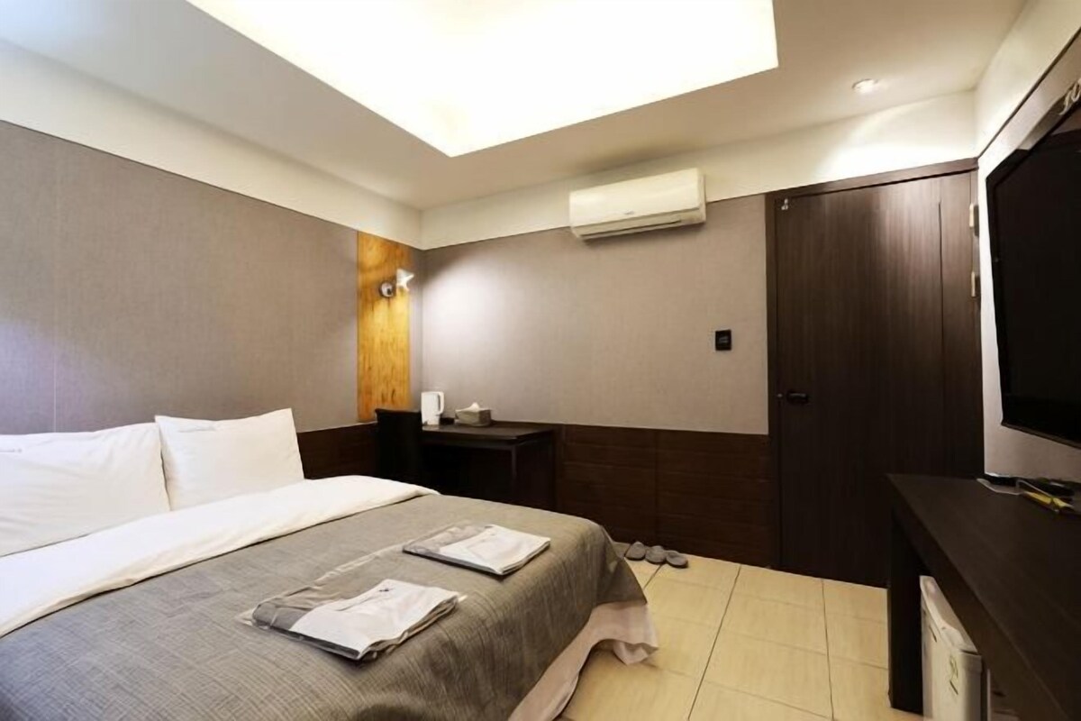 A hotel room with a bed, a TV, a wardrobe, and a window.