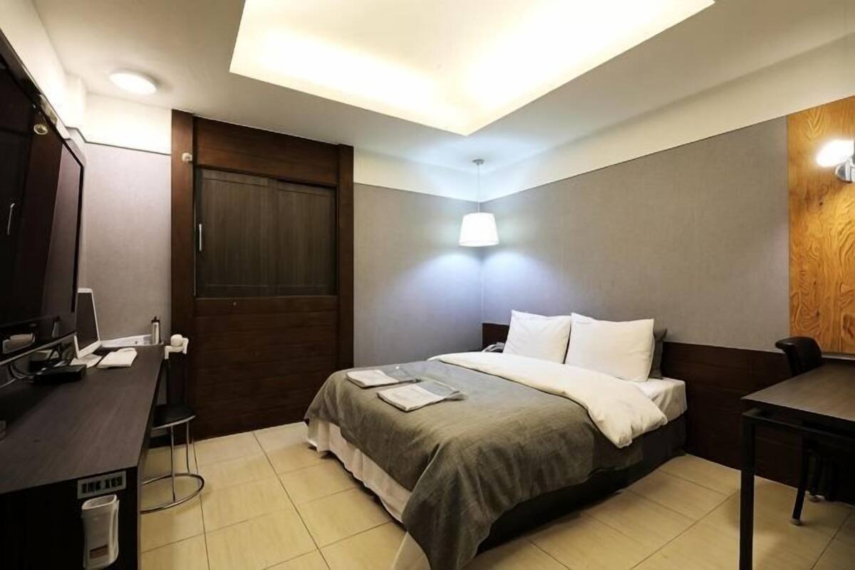 Una habitación de hotel con cama, escritorio, silla y una puerta de madera.