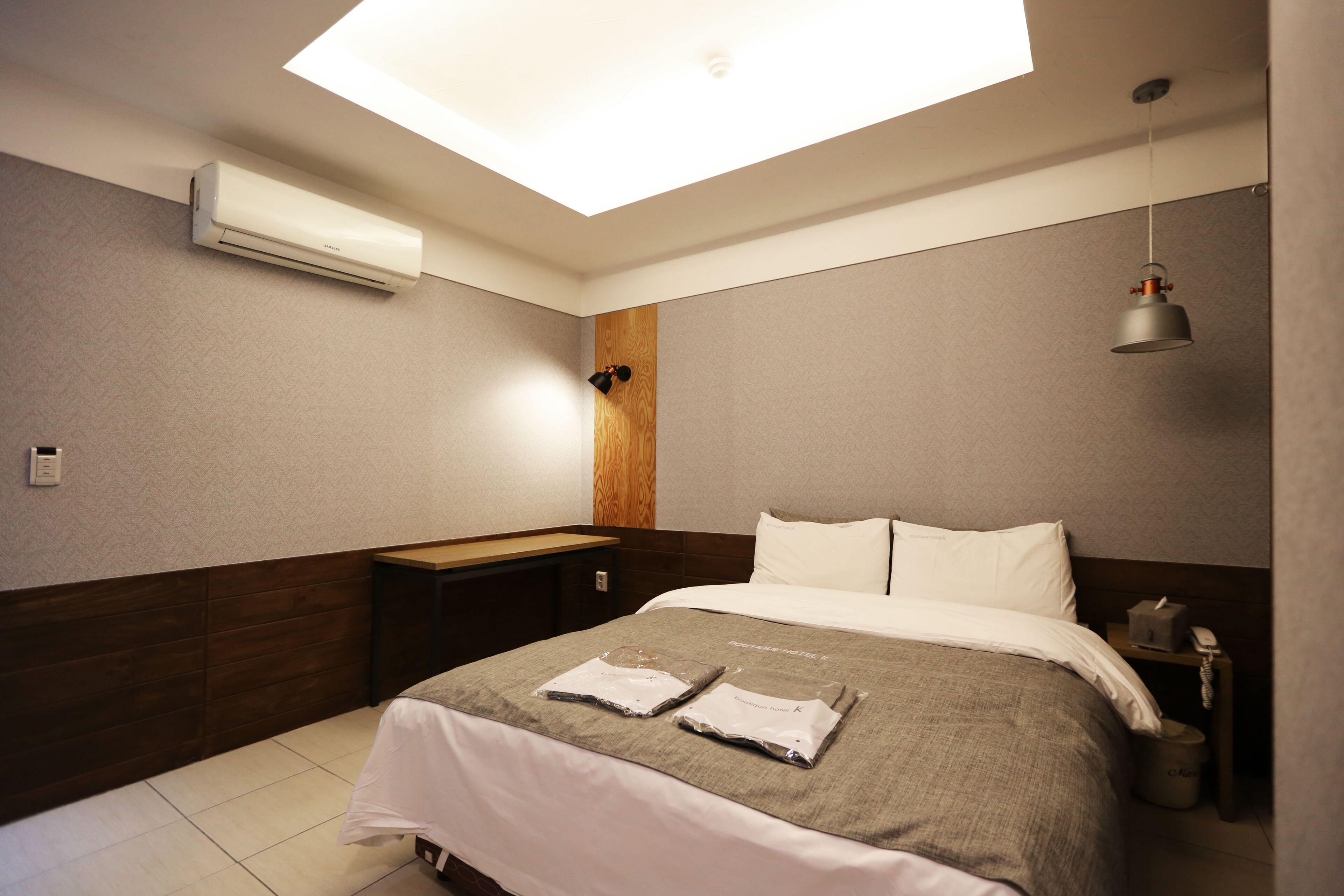 Een moderne hotelkamer met dakraam, een bed met keurig opgevouwen handdoeken, een nachtkastje en een bijzettafeltje met lamp.