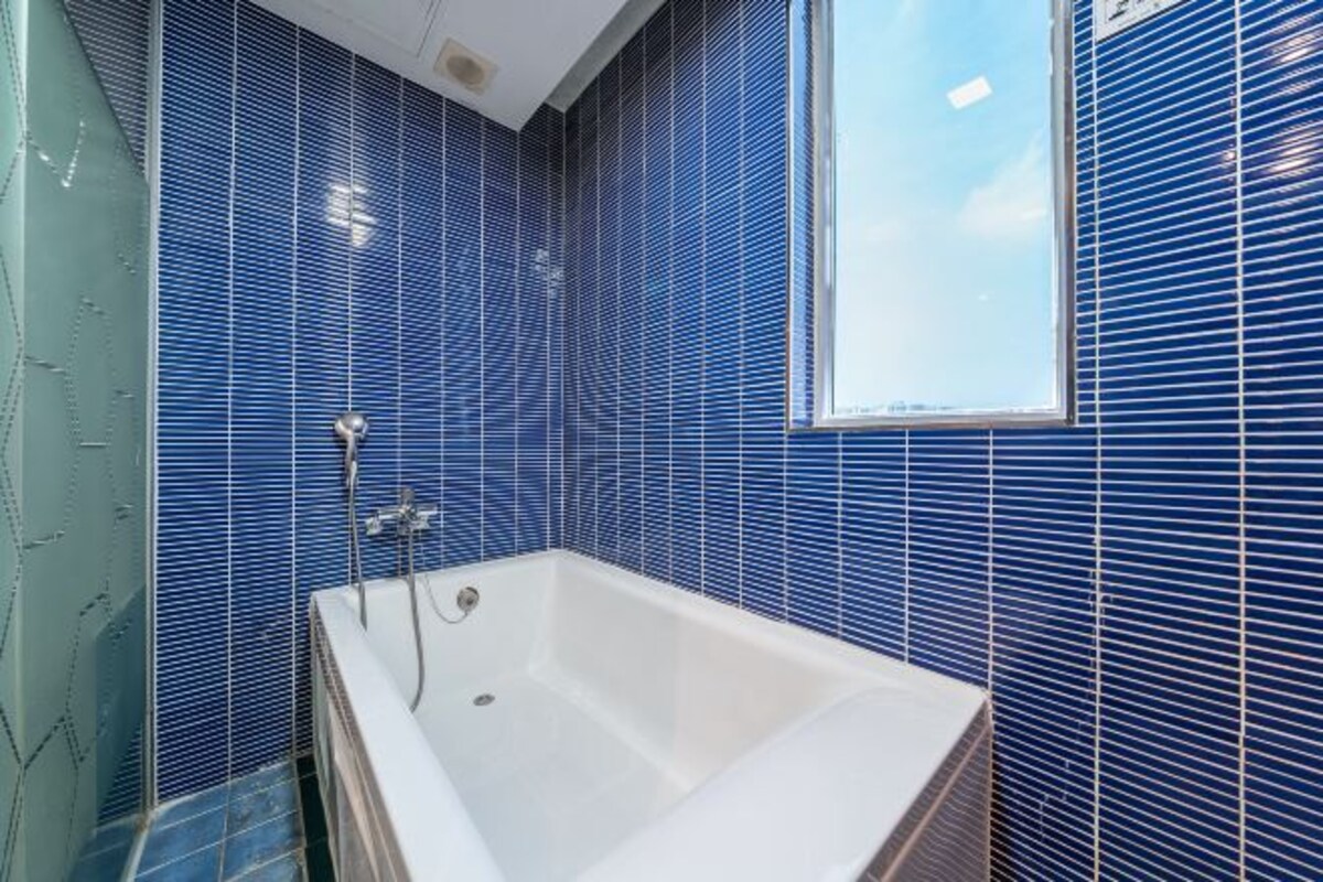 Een badkamer met een bad, blauwe betegelde wanden en een raam.