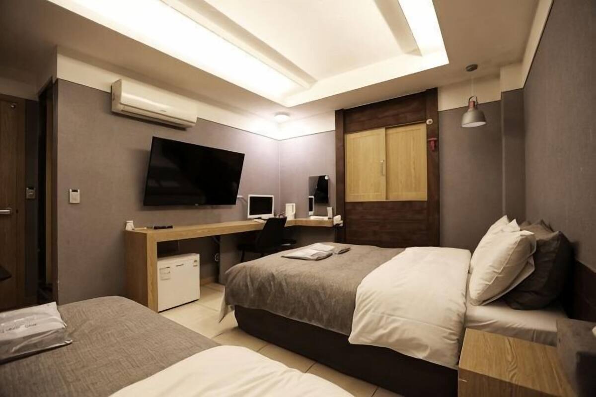 Habitación de hotel con cama, escritorio, televisor y una kitchenette pequeña.