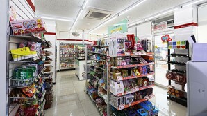 Une allée d’un supermarché bien éclairée, avec différents produits exposés sur les étagères, notamment des en-cas et des articles ménagers.