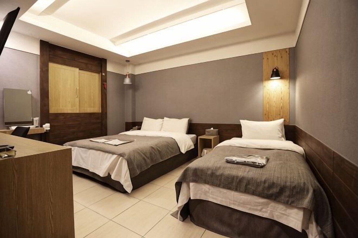 Ein Hotelzimmer mit zwei Betten, einem Schreibtisch, einem Spiegel und einer Deckenleuchte.