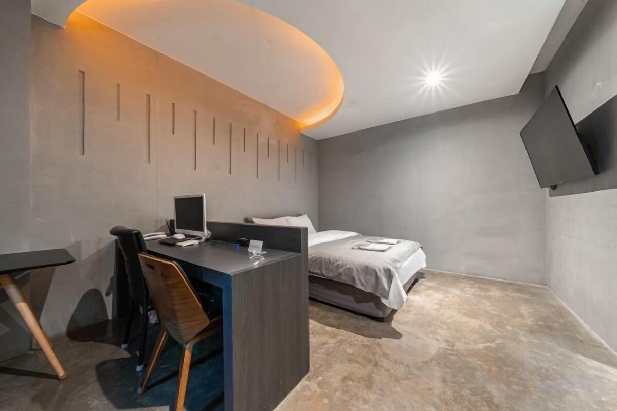 Una habitación de hotel moderna con escritorio, silla, cama y televisor de pantalla plana montado en la pared.