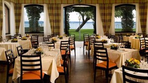 A dining area with tables set for service, large windows with a view of the outdoors, and a wooden floor. - Hotel Fonte Boiola (Sirmione)