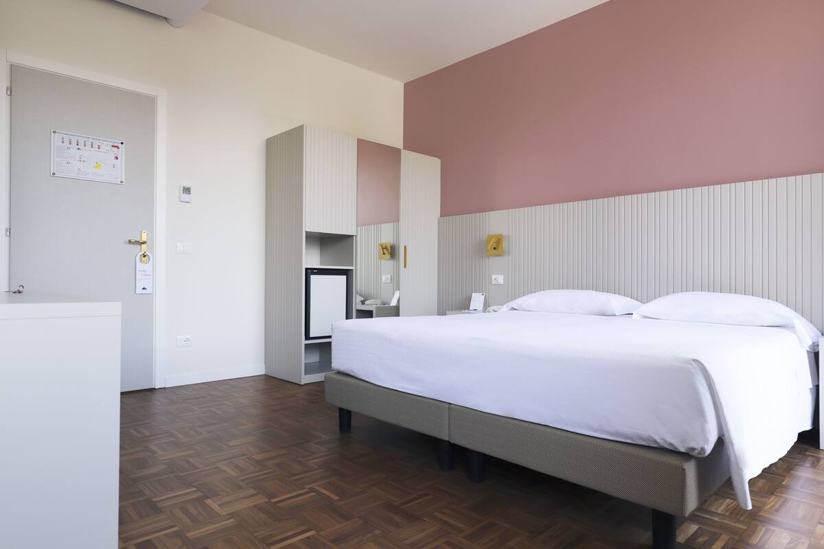 A hotel room with a bed, a desk, a chair, and a wardrobe.