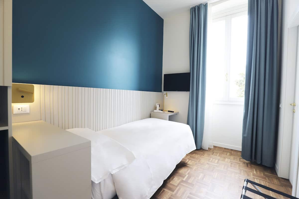 A hotel room with a bed, bedside table, lamp, and a window with curtains.