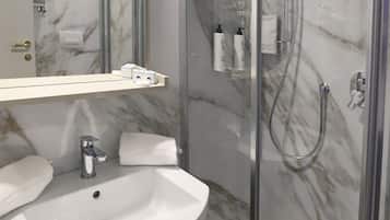 Een moderne badkamer met een marmeren achterwand, een witte wastafel, een douche met glazen wanden en een spiegel boven de wastafel.