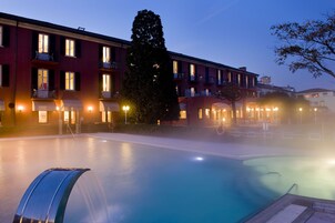 A hotel with a swimming pool, multiple balconies, and a well-lit facade.