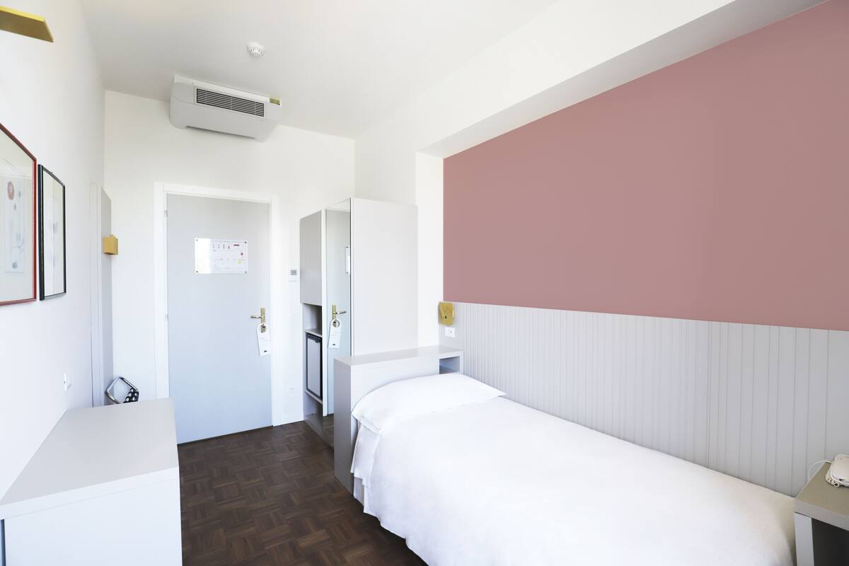A hotel room with a bed, bedside table, and a wall-mounted air conditioner.
