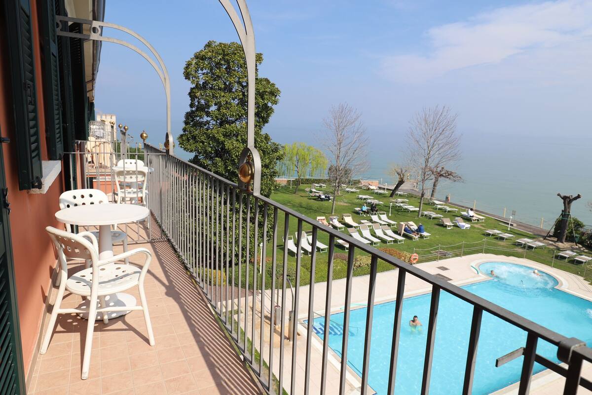 A balcony with a pool, lounge chairs, and a view of the lake.