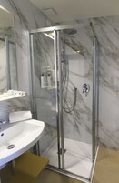 Ein modernes Badezimmer mit einer gläsernen Duschkabine, einem weißen Waschbecken und einer Marmor-Spritzschutzwand.