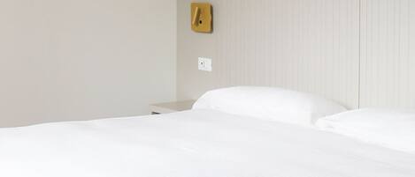 A hotel room with a bed, a nightstand, a wall socket, and a wall-mounted light switch.