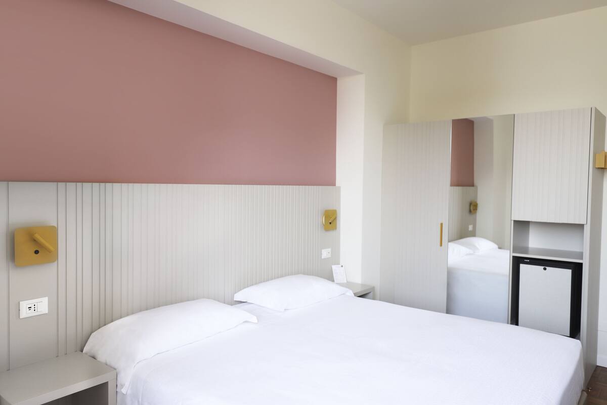 A hotel room with a large bed, a bedside table, a small desk, and a wardrobe.