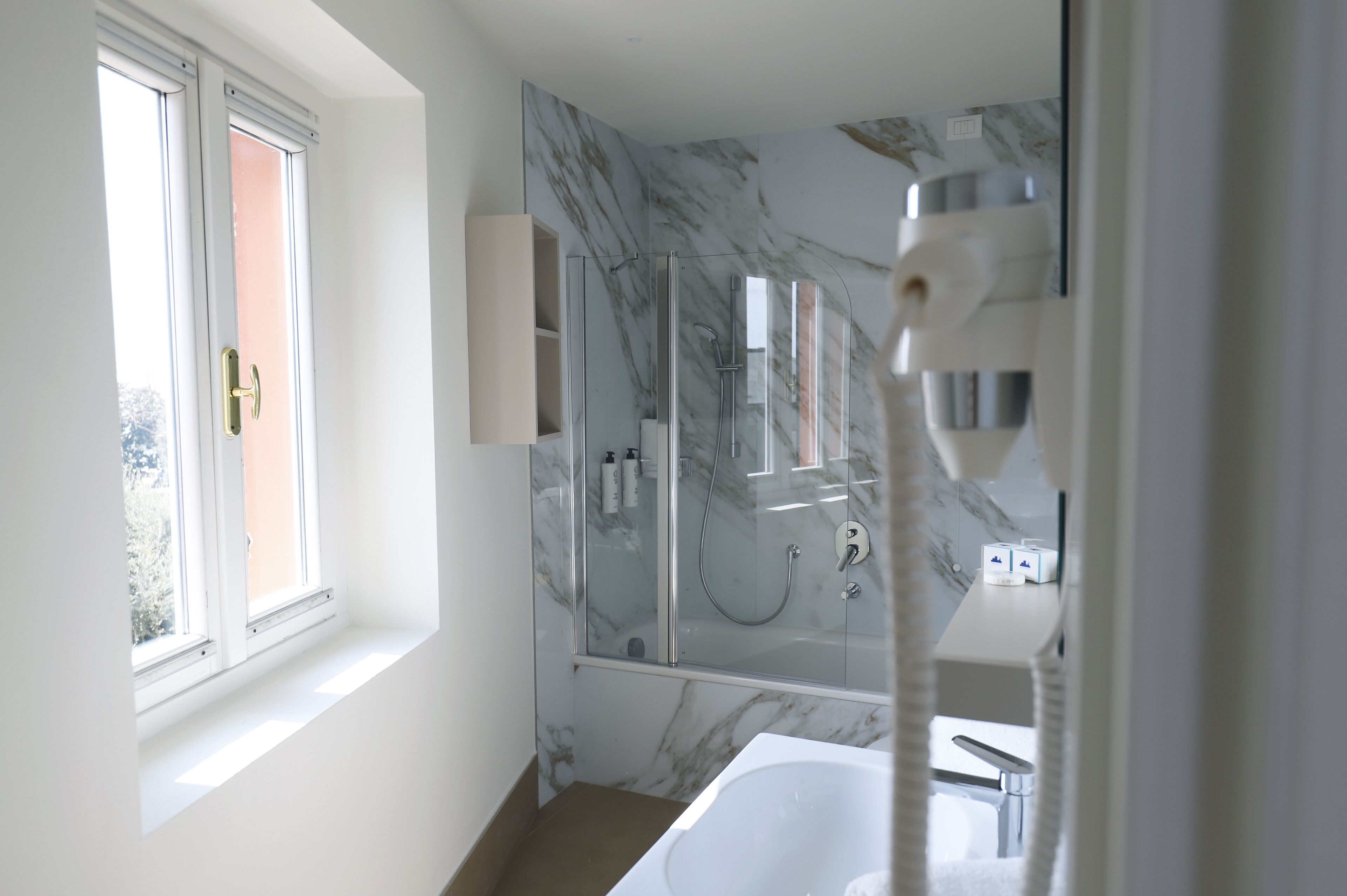 A modern bathroom with a glass-enclosed shower, a white bathtub, and a window providing natural light.