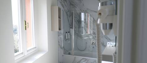 A modern bathroom with a glass-enclosed shower, a white bathtub, and a window providing natural light.