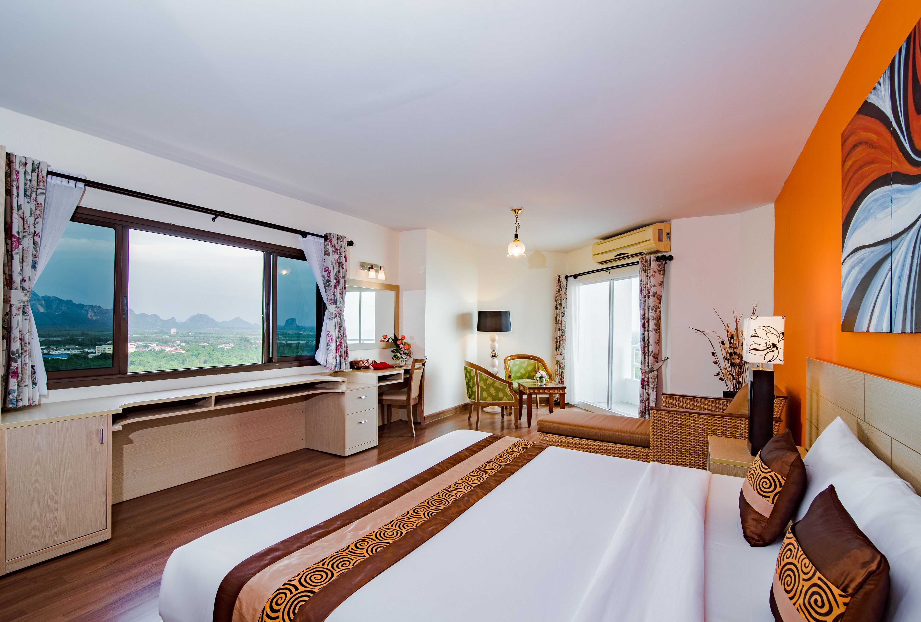 A hotel room with a large bed, a desk, a chair, and a view of the mountains.
