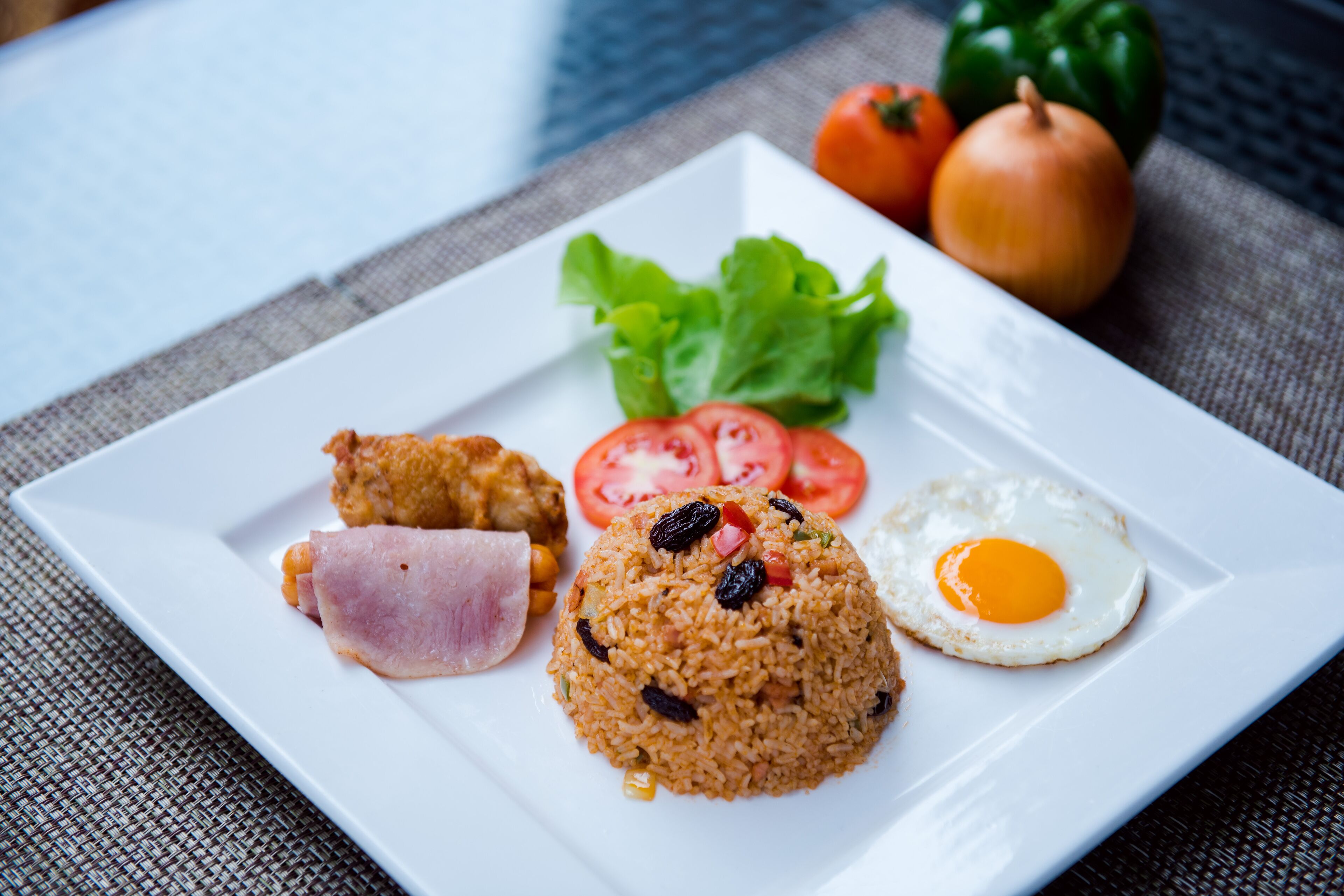 Un plato de comida con arroz, huevo, tomate, lechuga y jamón.