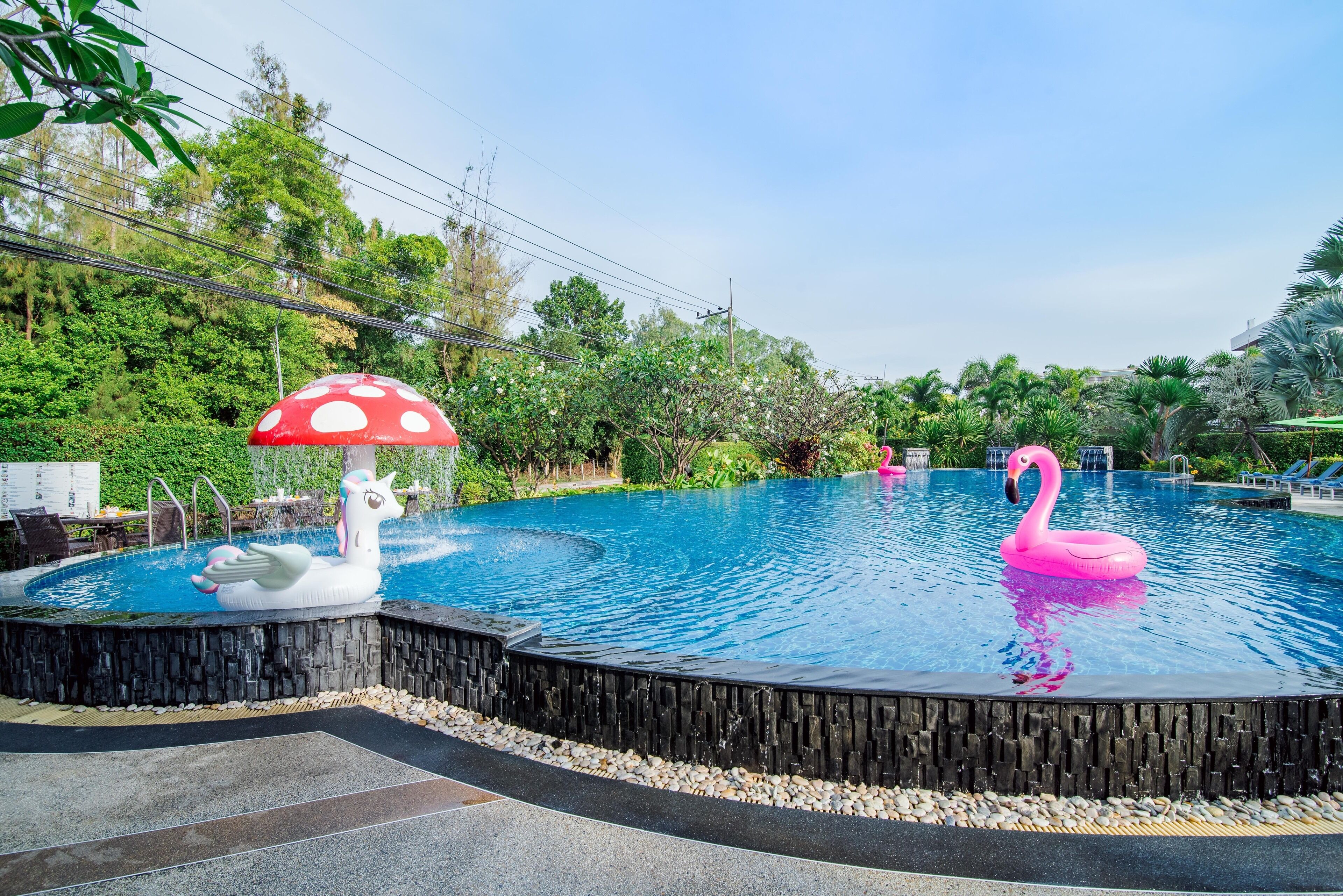 Piscina con un cisne blanco y un pato flamenco de inflable, rodeada de follaje y un muro de piedra.