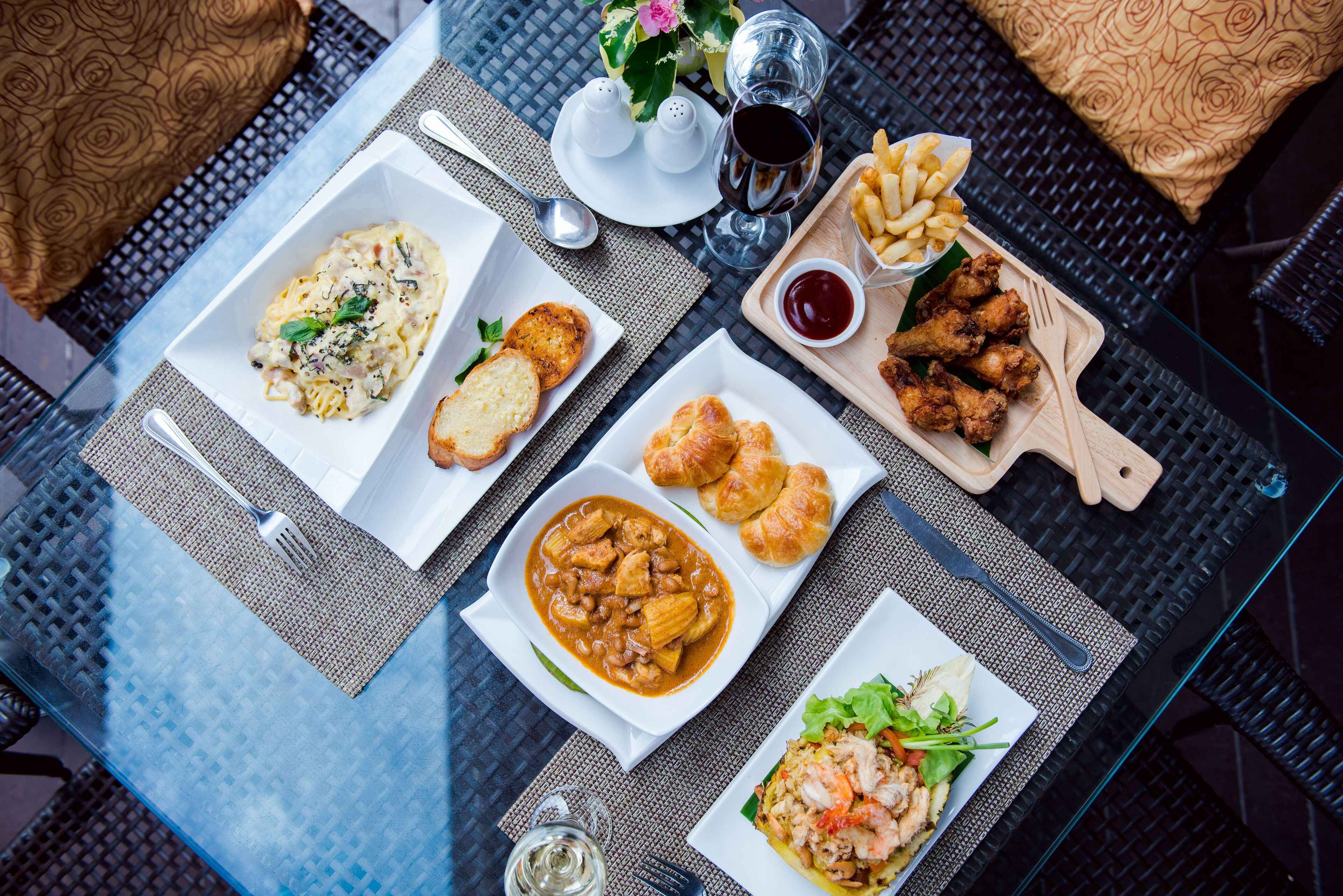 A dining table with various dishes, including pasta, chicken wings, and shrimp, along with condiments and drinks.