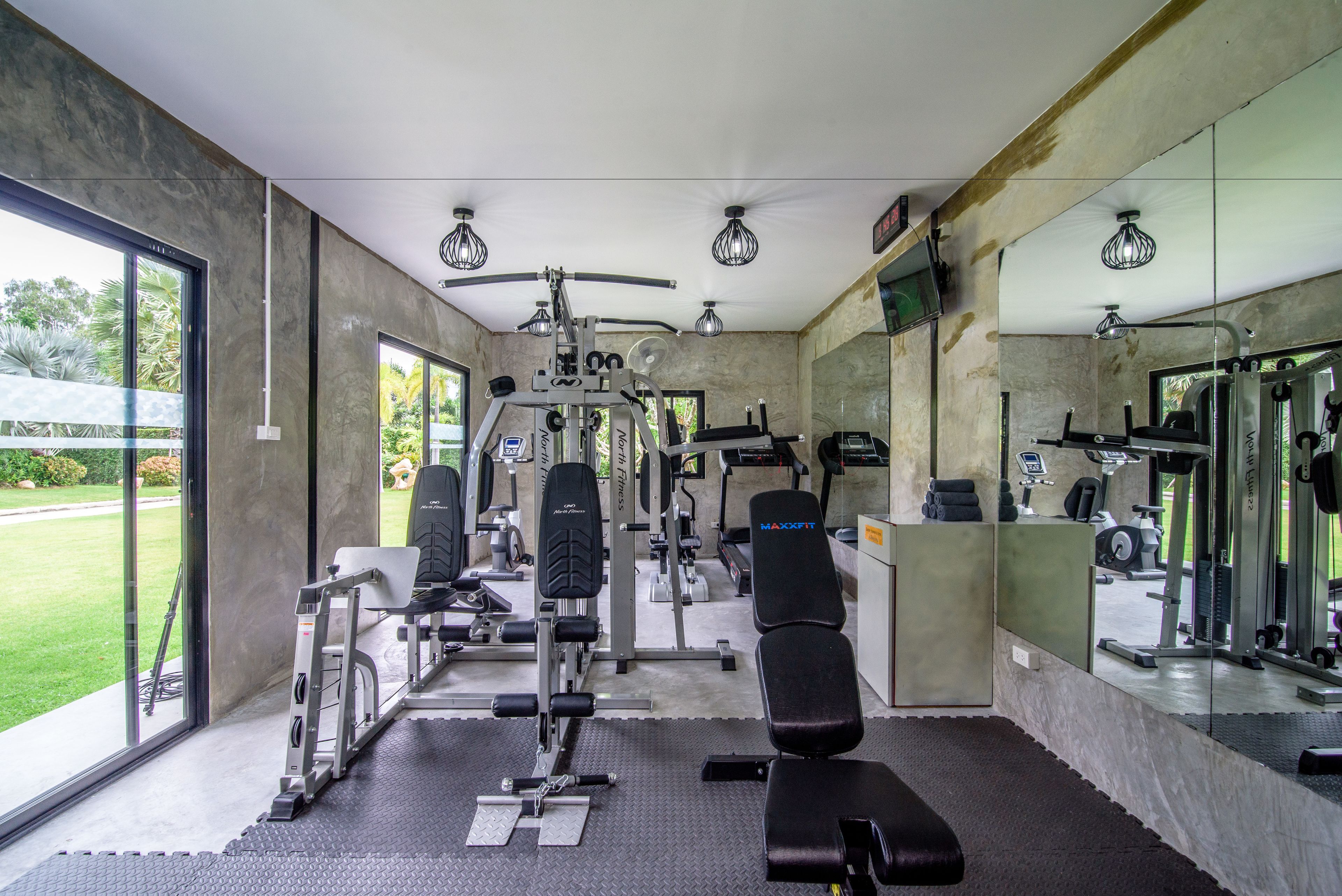 A gym with various exercise equipment, large windows, and a mirror wall.